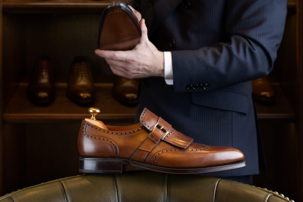 Pantof maro din piele naturală în fața unui afișaj din lemn în magazinul de pantofi pentru bărbați.