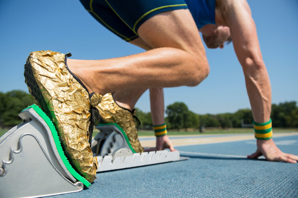 pantofi de sport aurii pe picioarele unui alergător care începe pe banda de alergare olimpică