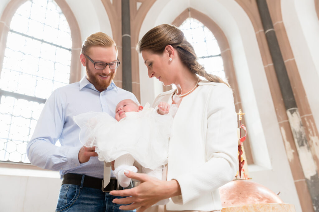 Tinerii părinți la biserică cu copilul lor purtând o rochie de botez