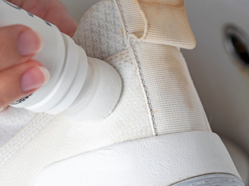 Curățarea unui preparat special cu un burete dintr-un pantof sport alb: elemente din piele
