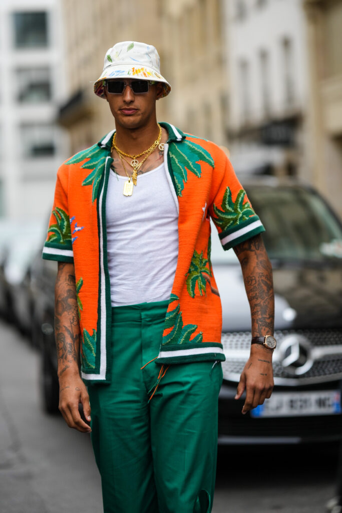 PARIS, FRANCE - JUNE 25: Kyle Kuzma wears a white with yellow and blue print pattern bob, sunglasses, gold long chain necklaces, a white ribbed tank-top, an orange with green leaves print pattern short sleeves open shirt, green flowing large pants, a black shiny leather watch, outside the Casablanca show, during Paris Fashion Week - Menswear Spring/Summer 2023, on June 25, 2022 in Paris, France. (Photo by Edward Berthelot/Getty Images)