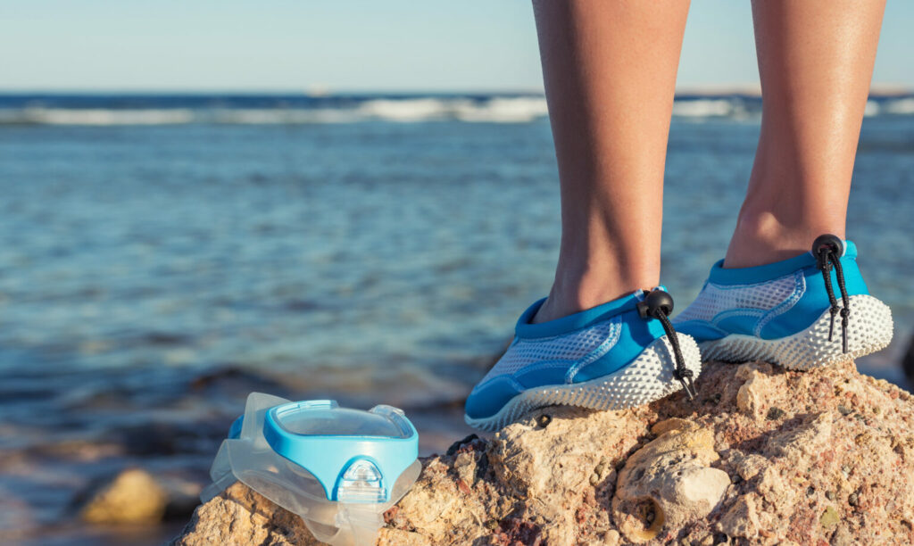 Persoană în picioare pe o stâncă pe malul mării, purtând pantofi de apă albastru