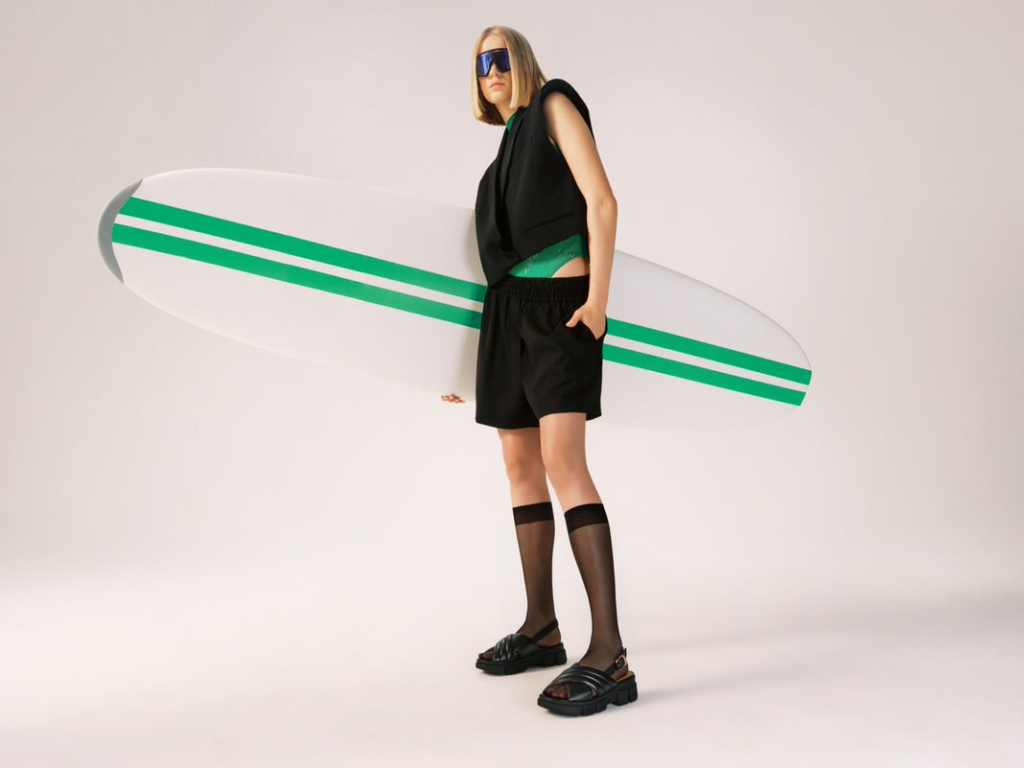 Model în total look negru, cu sandale negre, ținând în mână o placă de surf - Campania de vară 2023
