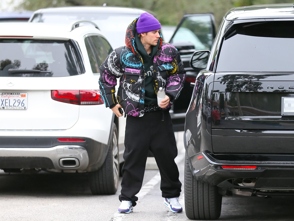 Justin Bieber poartă o căciulă mov, o geacă colorată și pantaloni de trening negri