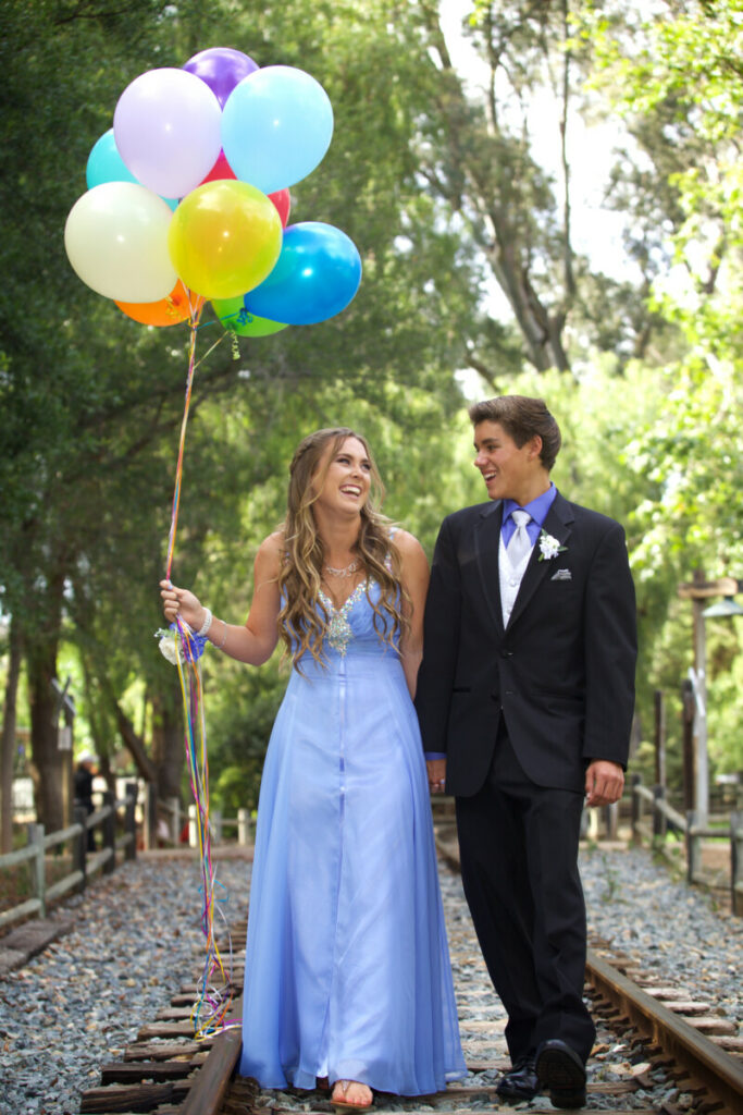Un cuplu de tineri care merg la o petrecere aniversară, îmbrăcați elegant, fata are un buchet de baloane în mână